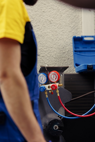 Adept repairman hired to check outdoor hvac system refrigerant tank in need of maintenance, using manometers. Licensed serviceman with ac gauges vacuum pump looking at air conditioner freon levels